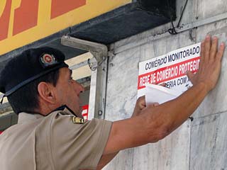 Policial colando cartaz da Rede de Comércios Protegidos