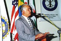 Foto de Waldir Francisco de Andrade fazendo discurso em frente ao microfone com bandeiras de v?rios pa?ses ao fundo