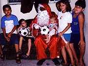 Carlos vestido de Papai Noel e entregando presente ?s crian?as