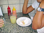 Foto de uma mulher comendo salgado e tomando suco
