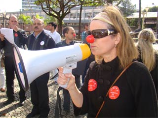 Mulher protestando com nariz de palhaço e megafone