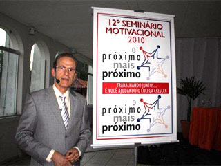Armando Falconi ao lado de uma banner sobre semin&aacute;io motivacional